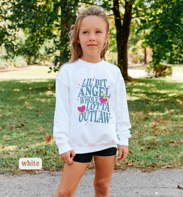 A young girl wearing a white sweatshirt with text printed on it, standing in a park surrounded by trees.